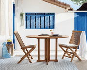 Zwei Holzklappstühle und ein runder Holztisch in einem mediterranen Außenbereich, seitliche Perspektive