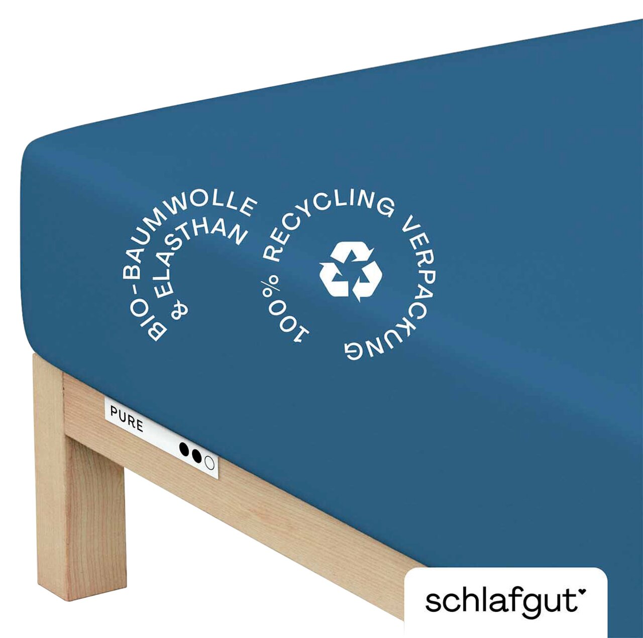 schlafgut Spannbettlaken S 615 Pure Blaues Spannbettlaken aus Bio-Baumwolle und Elasthan, auf einer Matratze von schräg oben fotografiert, mit Hinweis auf 100% Recycling-Verpackung.