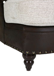 Nahaufnahme eines Megaohrensessels mit dunkelbraunem Lederbezug, heller Sitzfläche und dekorativen Nieten. Perspektive von der Seite.