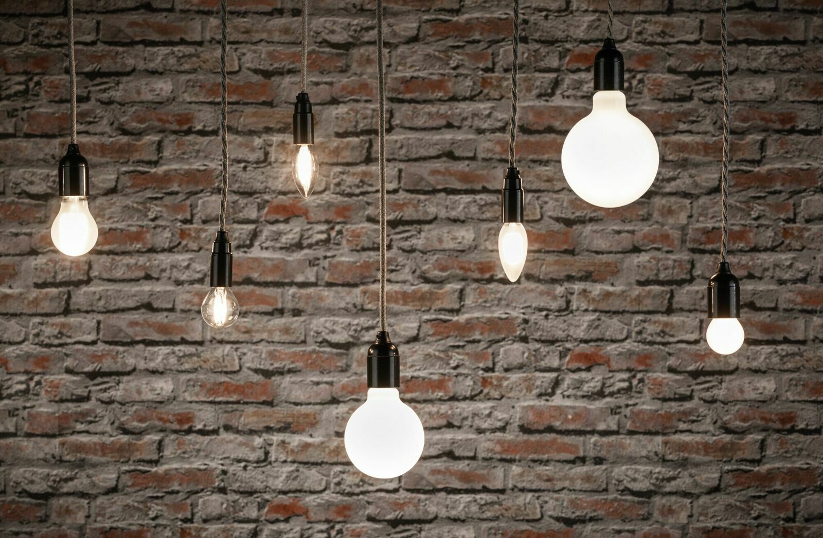 Verschiedene hängende LED-Leuchtmittel vor einer Ziegelwand, aus seitlicher Perspektive fotografiert.