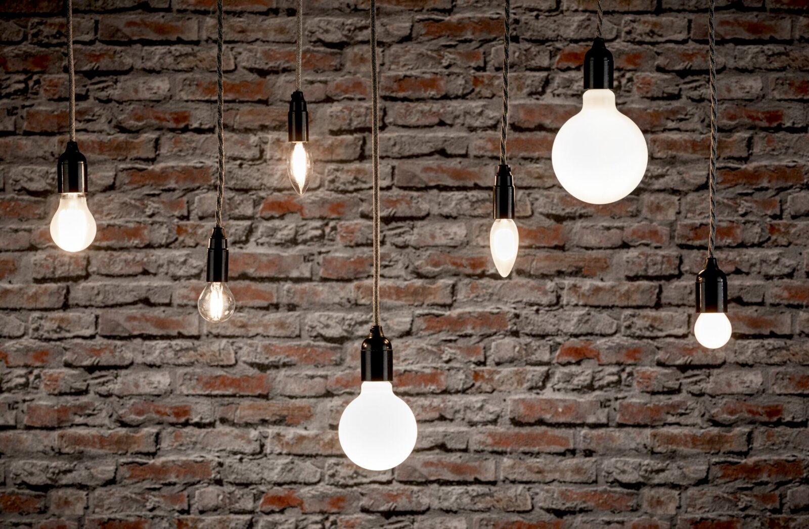 Verschiedene hängende LED-Leuchtmittel vor einer Ziegelwand, aus seitlicher Perspektive fotografiert.
