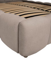 Nahaufnahme eines Polsterbettgestells in Beige mit sichtbaren Holzlatten, seitliche Perspektive.
