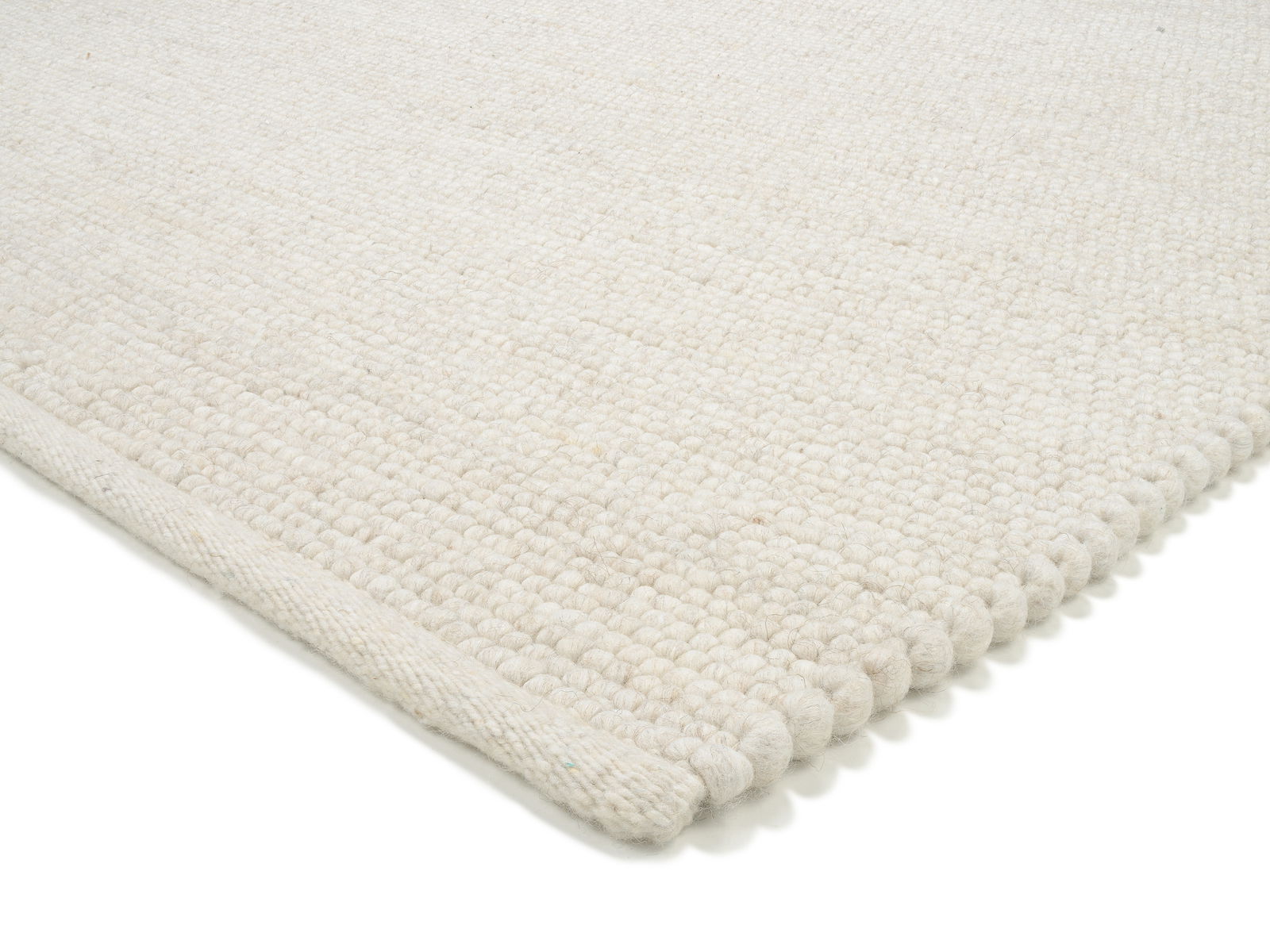 Nahaufnahme eines weißen, handgewebten Teppichs mit strukturierter Oberfläche, von der Seite fotografiert.