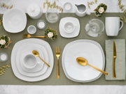 Draufsicht auf modern gedeckten Tisch mit weißem quadratischem Porzellan-Geschirr (Teller, Schalen, Tassen), Glaswaren und goldfarbenem Besteck auf grünem Tischläufer, dekoriert mit Kerzen und kleinen Blumenarrangements