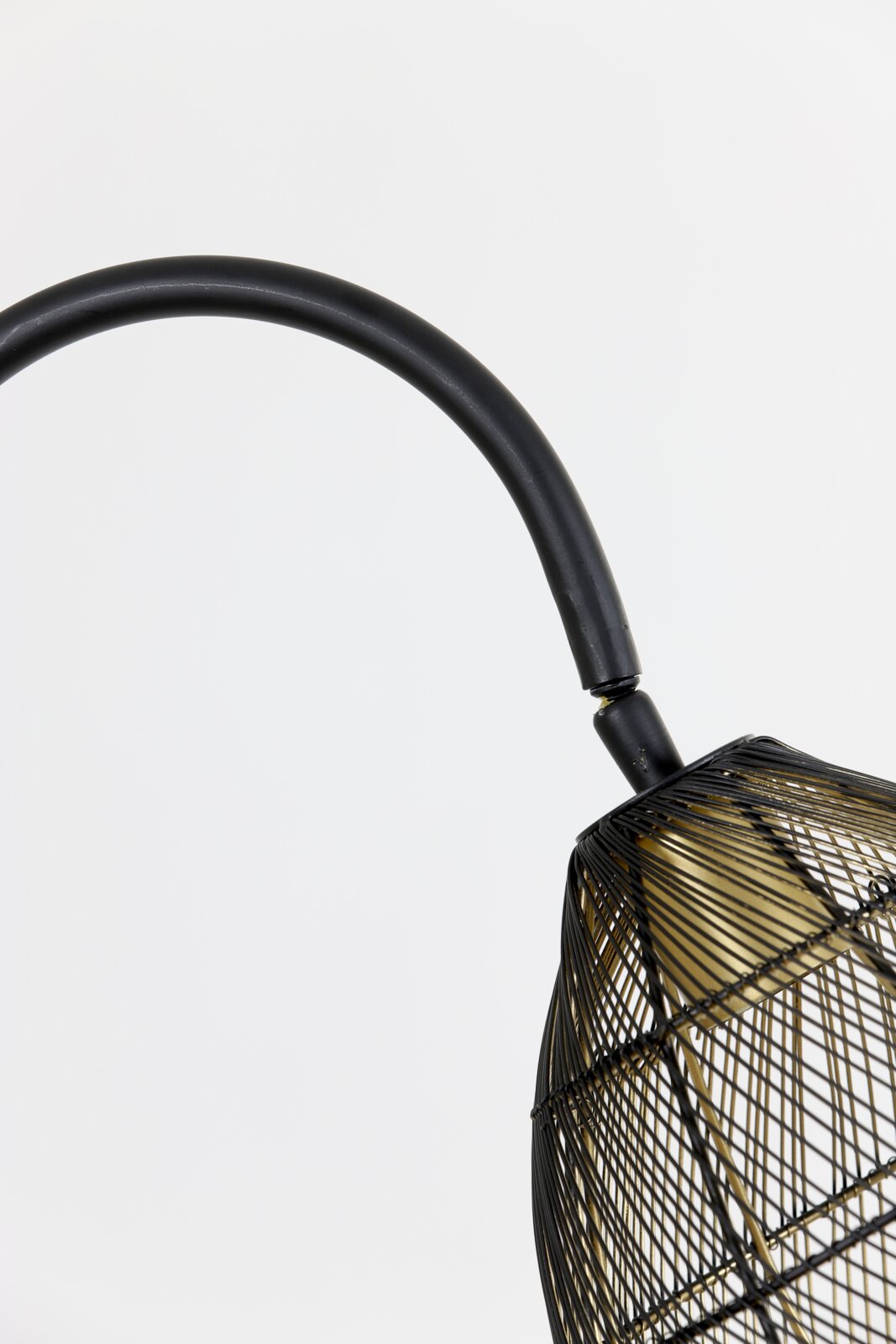 Detailopname van opzij en licht van onderen van een zwarte lamp met gebogen arm en open draadkap met goudkleurige binnenzijde.