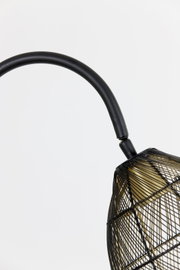 Detailopname van opzij en licht van onderen van een zwarte lamp met gebogen arm en open draadkap met goudkleurige binnenzijde.