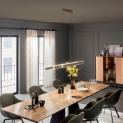 Moderne, lineare LED-Pendelleuchte in Weiß über einem langen Holzesstisch im Esszimmer, seitliche Perspektive mit leichtem Blick von unten.