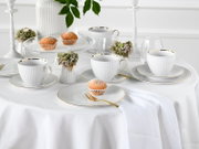 Schick gedeckter Tisch mit weißem geripptem Porzellan-Kaffeeservice mit Goldrand (Tassen, Untertassen und Dessertteller), goldfarbenem Besteck und Muffins; Perspektive: leicht erhöhte Frontansicht schräg von vorn.