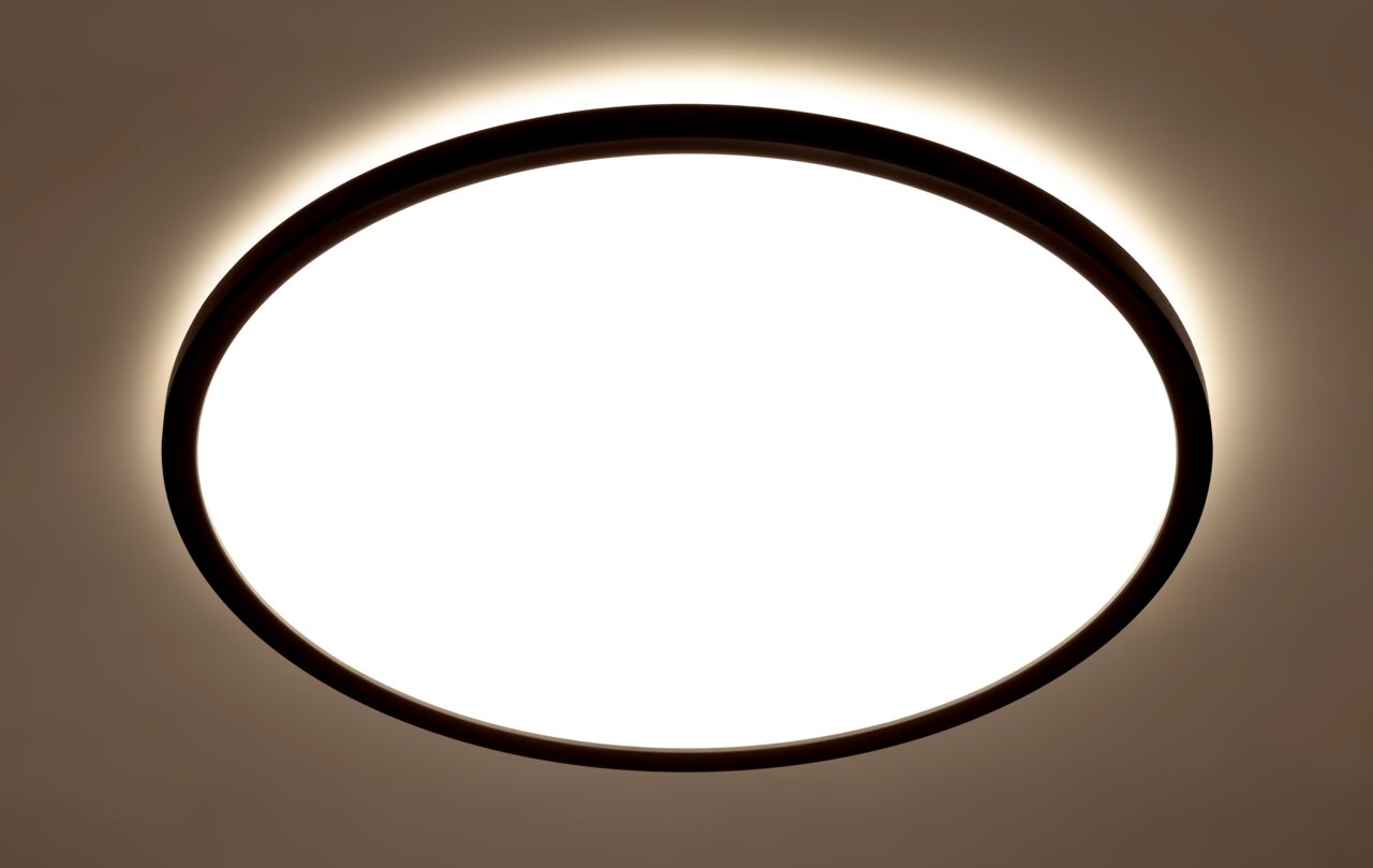 Runde LED-Deckenleuchte mit schwarzem Rahmen, von unten betrachtet, leuchtet hell mit einem sanften Lichtschein an der Decke.