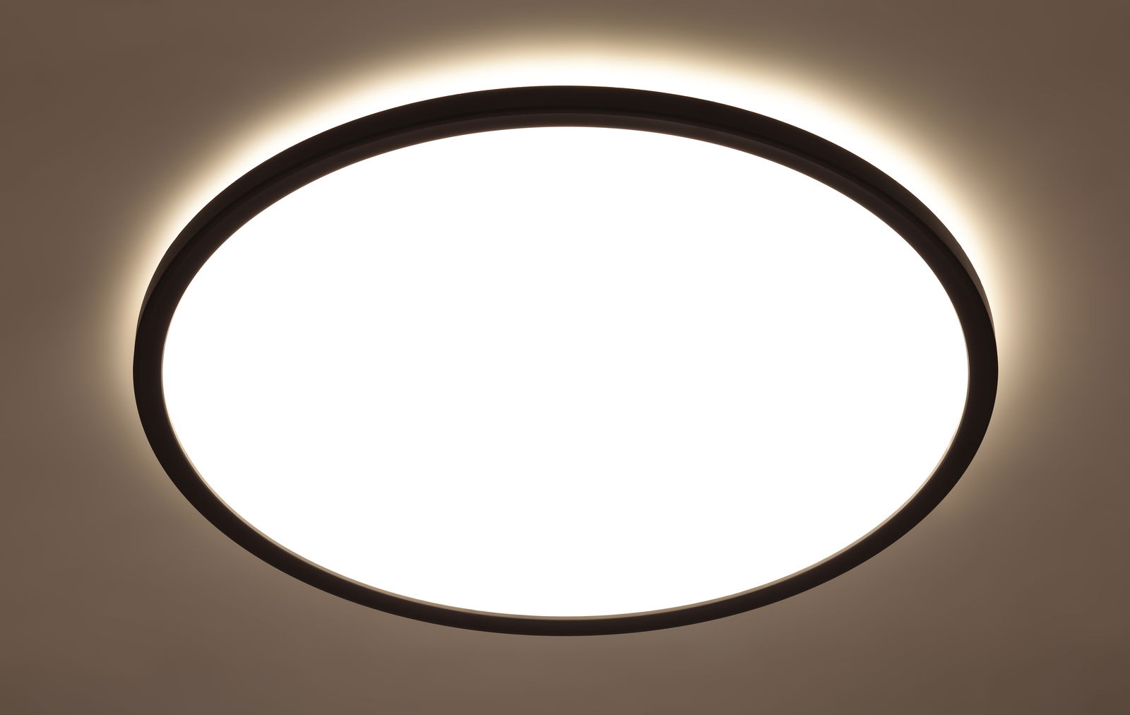 Runde LED-Deckenleuchte mit schwarzem Rahmen, von unten betrachtet, leuchtet hell mit einem sanften Lichtschein an der Decke.