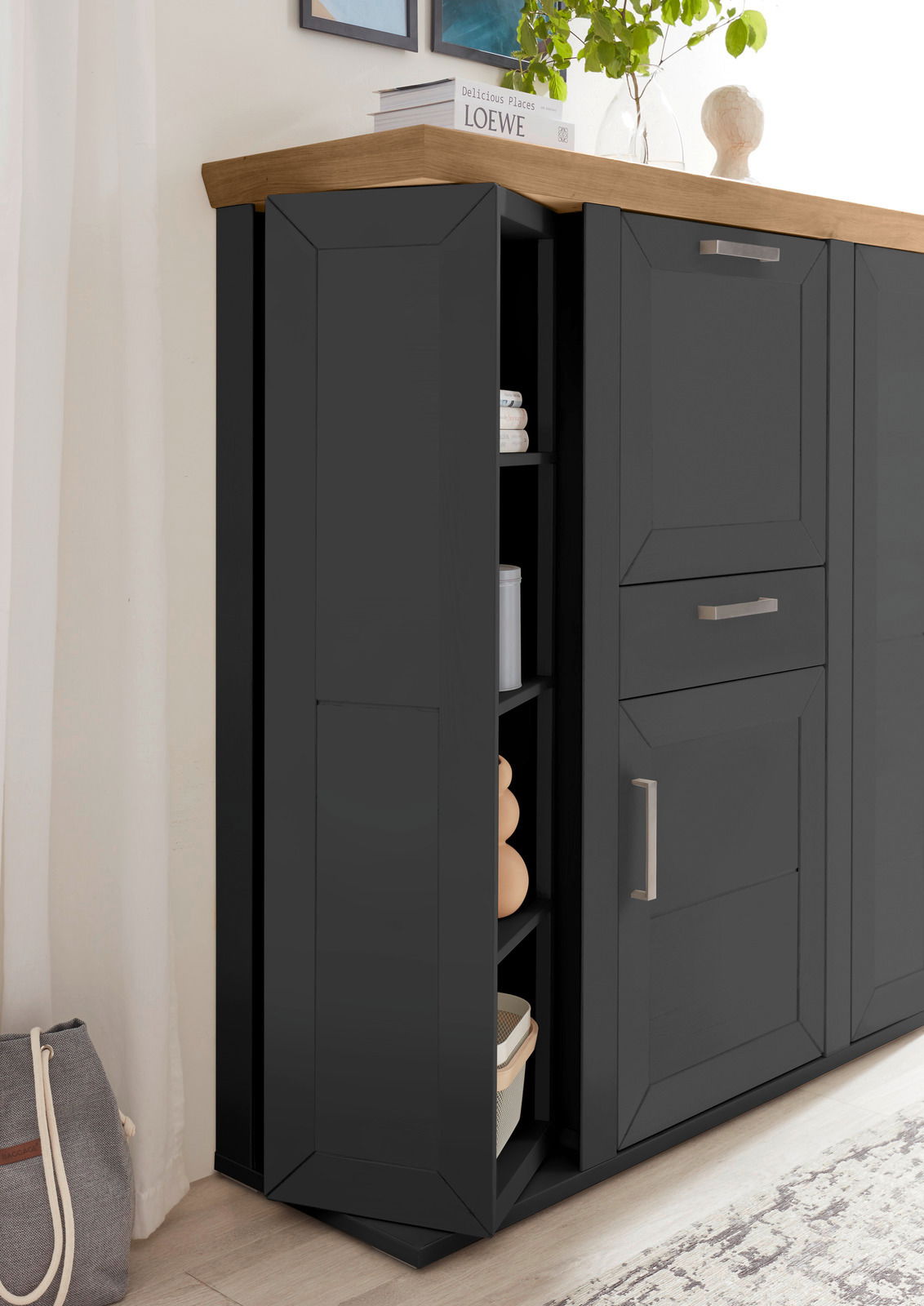 Schwarzes Highboard mit Karussellfunktion, seitliche Perspektive, mit Holzplatte und modernen Griffen, dekoriert mit Pflanzen und Büchern.