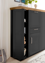Schwarzes Highboard mit Karussellfunktion, seitliche Perspektive, mit Holzplatte und modernen Griffen, dekoriert mit Pflanzen und Büchern.