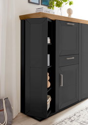 Schwarzes Highboard mit Karussellfunktion, seitliche Perspektive, mit Holzplatte und modernen Griffen, dekoriert mit Pflanzen und Büchern.