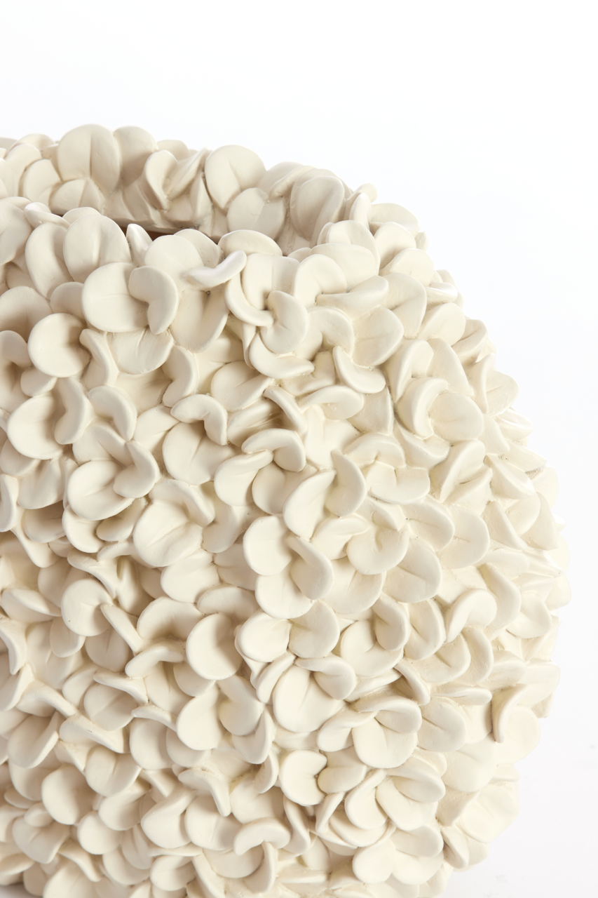 Nahaufnahme einer weißen Vase mit blütenblattartiger Struktur, seitliche Perspektive.