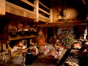 Gemütliche Weihnachtsstimmung in einer rustikalen Holzhütte mit Kaminfeuer, geschmücktem Weihnachtsbaum und festlich gedecktem Tisch mit Bechern. Perspektive: Innenansicht des Wohnzimmers.