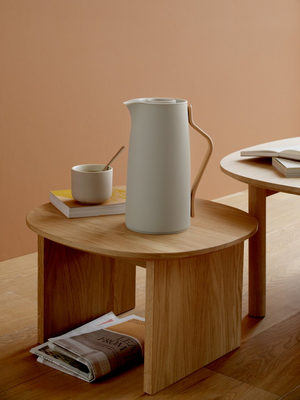 Elegante Emma Isolierkanne in modernem Design, seitliche Perspektive auf einem Holztisch mit Tasse und Büchern.
