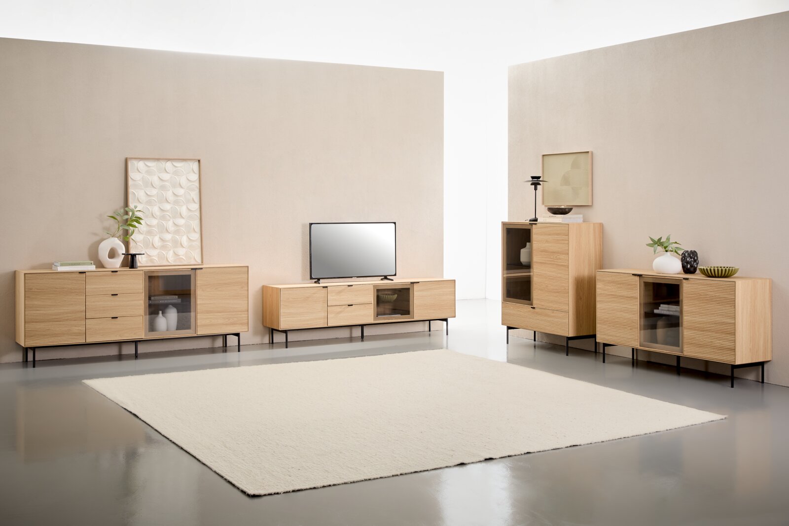XORA TV-Lowboard BORA Modernes Wohnzimmer-Setup mit hellen Sideboards und TV-Lowboard aus Holz mit gerillten Fronten, schwarzen Metallfüßen und Glaselementen, dekoriert mit Vasen und Bildern; Perspektive: frontale, leicht erhöhte Weitwinkelansicht.