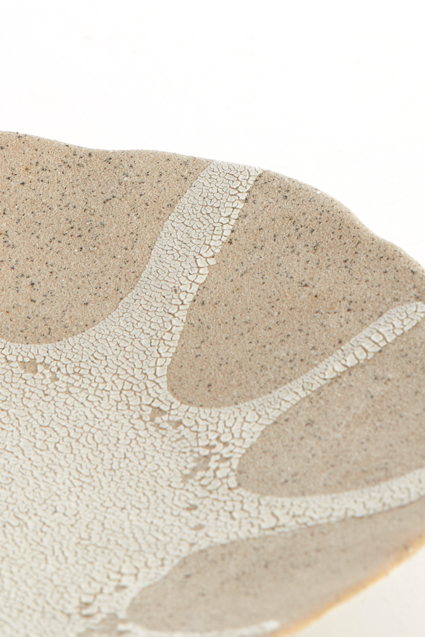 Detailaufnahme aus schräger Draufsicht: beige-weiß gesprenkelte Keramikschale mit craquelierter Glasur und organischem Muster auf weißem Hintergrund