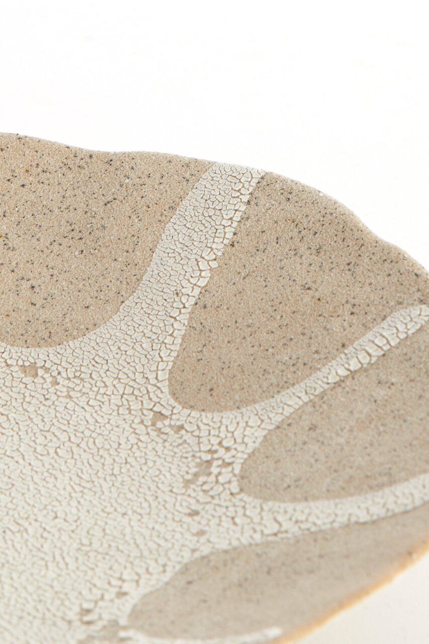 Detailaufnahme aus schräger Draufsicht: beige-weiß gesprenkelte Keramikschale mit craquelierter Glasur und organischem Muster auf weißem Hintergrund