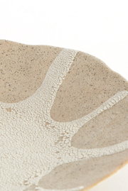 Detailaufnahme aus schräger Draufsicht: beige-weiß gesprenkelte Keramikschale mit craquelierter Glasur und organischem Muster auf weißem Hintergrund