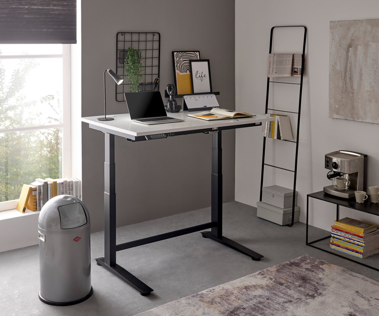 Modern, in hoogte verstelbaar elektrisch bureau in een stijlvol kantoor, gezien vanuit de zijkant, voorzien van een laptop, een lamp en decoraties.