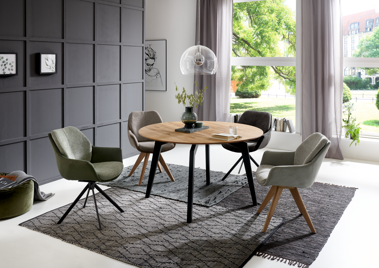 Valnatura Armlehnstuhl MANADO Moderner Essbereich mit rundem Holztisch und vier Armlehnstühlen in verschiedenen Farben, seitliche Perspektive.