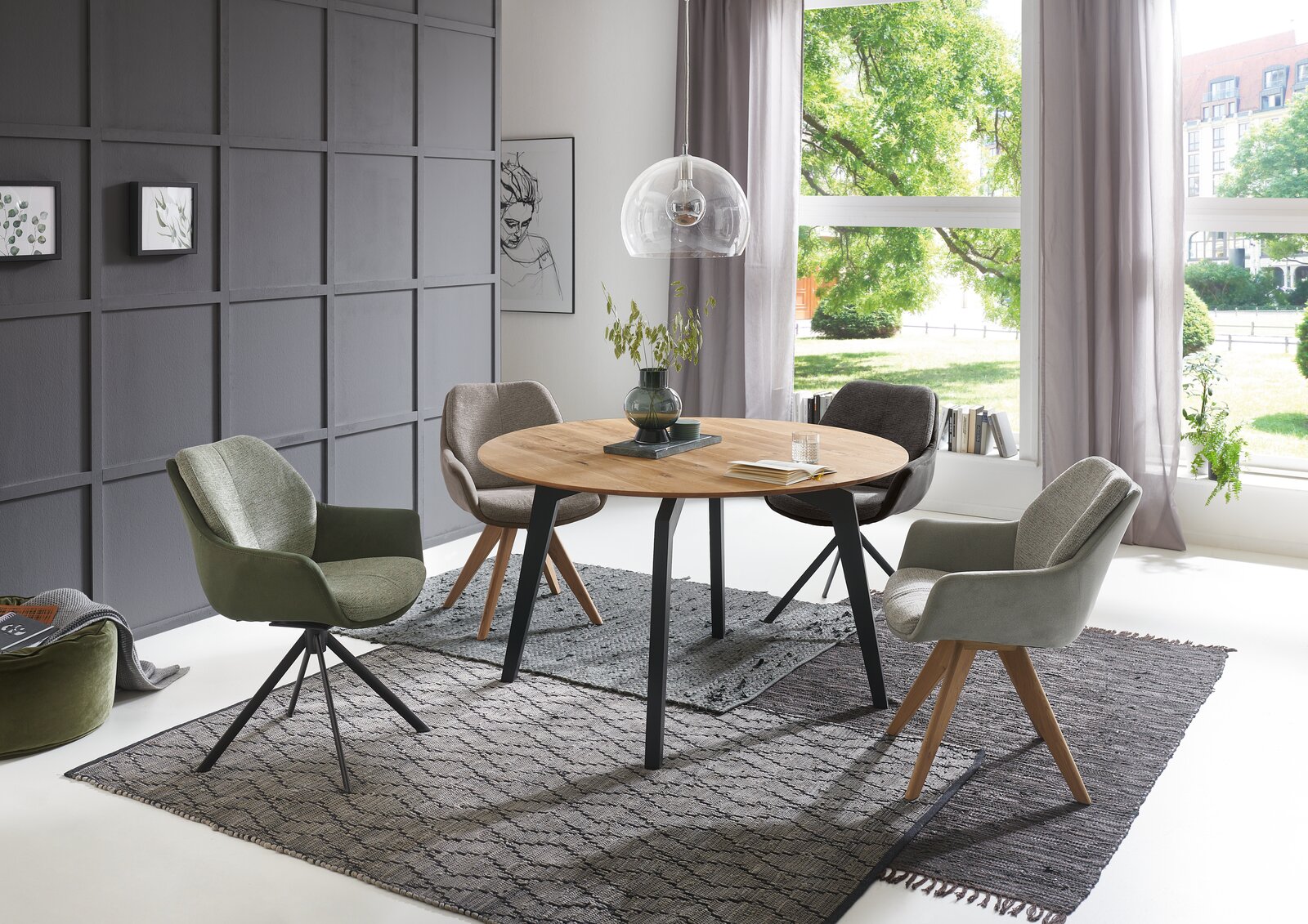 Valnatura Armlehnstuhl MANADO Moderner Essbereich mit rundem Holztisch und vier Armlehnstühlen in verschiedenen Farben, seitliche Perspektive.