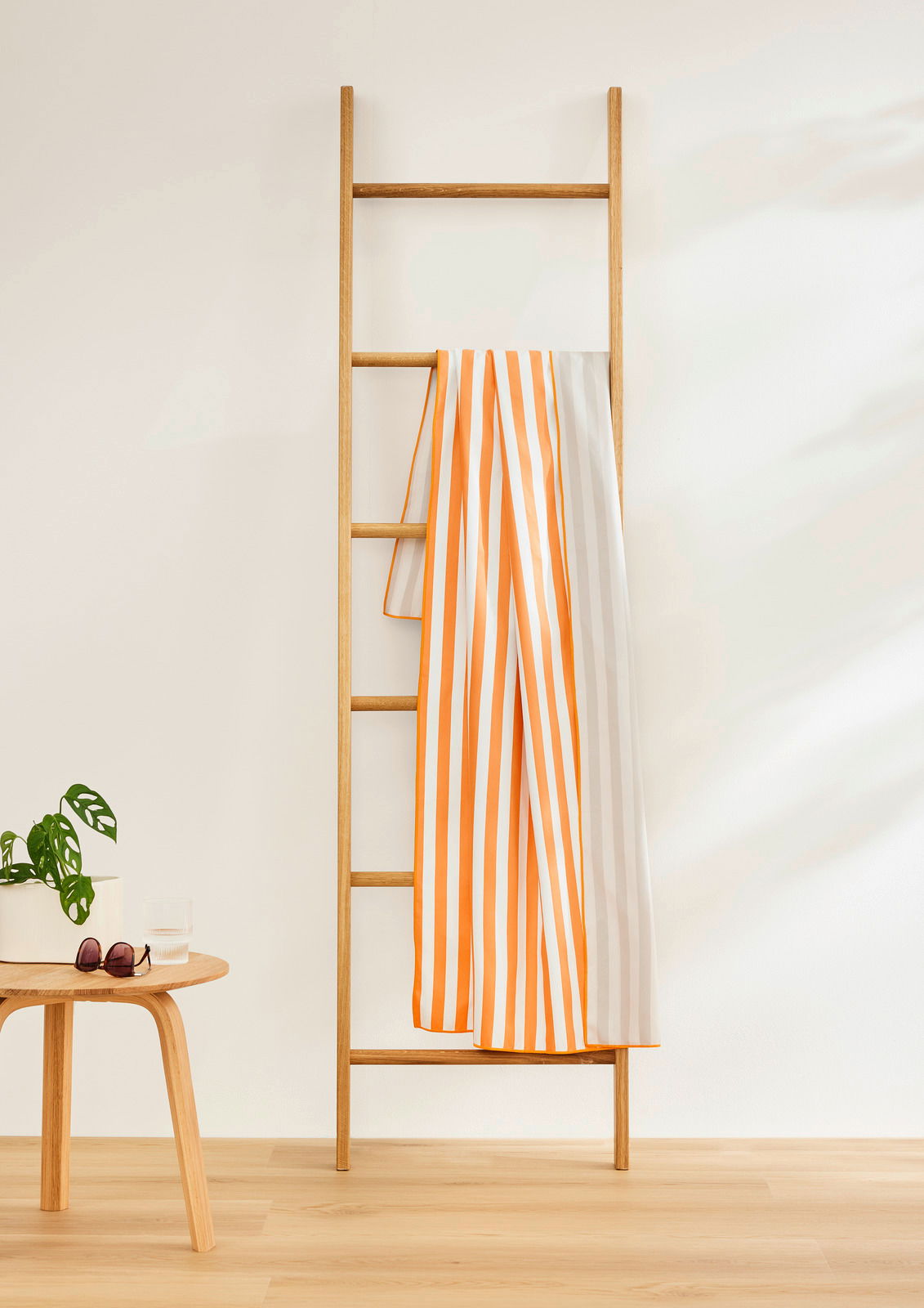 Gestreiftes Sporttuch in Orange und Weiß, drapiert über eine Holzleiter, seitliche Perspektive