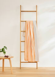 Gestreiftes Sporttuch in Orange und Weiß, drapiert über eine Holzleiter, seitliche Perspektive