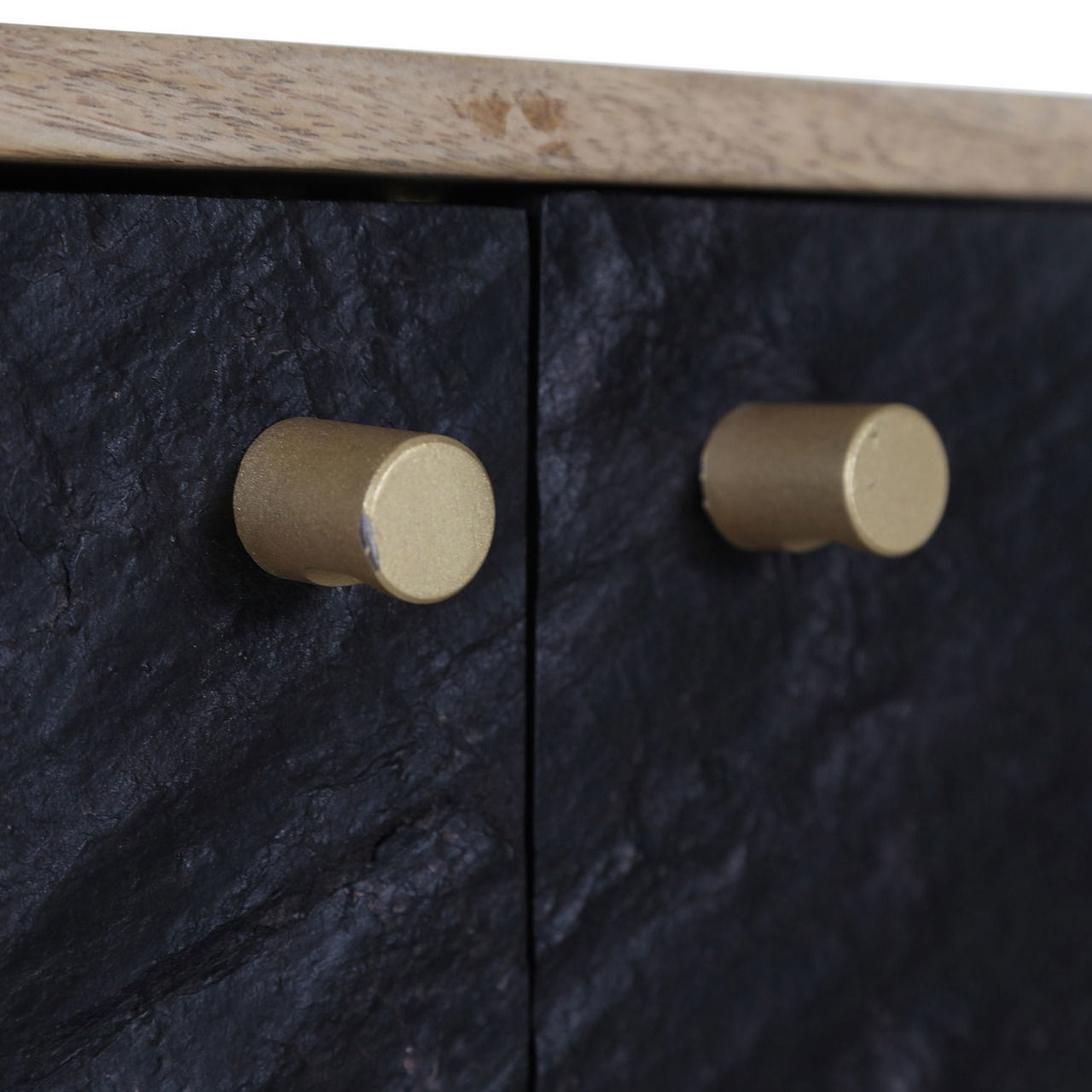 Nahaufnahme von zwei goldenen Knöpfen auf einer schwarzen, strukturierten Oberfläche eines TV-Lowboards, seitliche Perspektive