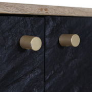 Nahaufnahme von zwei goldenen Knöpfen auf einer schwarzen, strukturierten Oberfläche eines TV-Lowboards, seitliche Perspektive