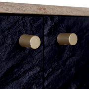 Nahaufnahme von zwei goldenen Knöpfen auf einer schwarzen, strukturierten Oberfläche eines TV-Lowboards, seitliche Perspektive