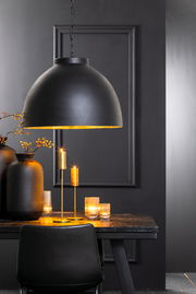 Schwarze Hängeleuchte mit goldener Innenseite über einem Tisch, umgeben von Kerzen und Vasen, seitliche Perspektive.