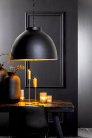 Schwarze Hängeleuchte mit goldener Innenseite über einem Tisch, umgeben von Kerzen und Vasen, seitliche Perspektive.