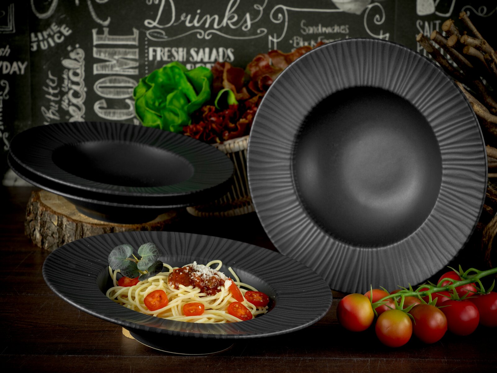 Schwarzes, geriffeltes Teller- und Schüssel-Set aus Keramik/Porzellan mit Pastaschale und Speisetellern auf rustikalem Holztisch, fotografiert in schräger Vorderansicht.