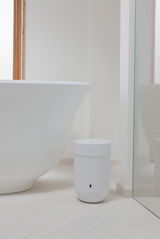 Weißer Mülleimer mit Deckel, im Badezimmer neben einer Badewanne platziert, aus seitlicher Perspektive fotografiert.