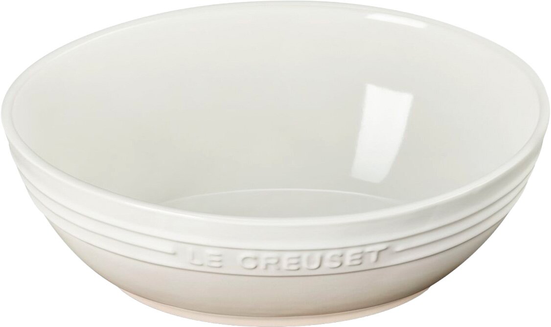 Weiße Keramikschüssel mit eingeprägtem „Le Creuset“-Schriftzug am Rand, freigestellt auf weißem Hintergrund, Perspektive: leicht von oben in 3/4-Ansicht.