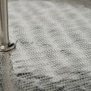 Nahaufnahme einer strukturierten, silbernen Oberfläche mit einem Metallstab, perspektivisch von der Seite betrachtet.