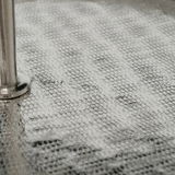 Nahaufnahme einer strukturierten, silbernen Oberfläche mit einem Metallstab, perspektivisch von der Seite betrachtet.