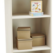 Weißes Standregal mit zwei Regalböden, darauf befinden sich Bücher und braune Aufbewahrungsboxen, seitliche Perspektive