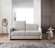 Modernes Schlafsofa in hellem Beige, frontal fotografiert, mit eleganten Armlehnen und einem gemütlichen Design, platziert in einem stilvollen Wohnzimmer mit Lampe und Beistelltischen.