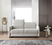 Modernes Schlafsofa in hellem Beige, frontal fotografiert, mit eleganten Armlehnen und einem gemütlichen Design, platziert in einem stilvollen Wohnzimmer mit Lampe und Beistelltischen.