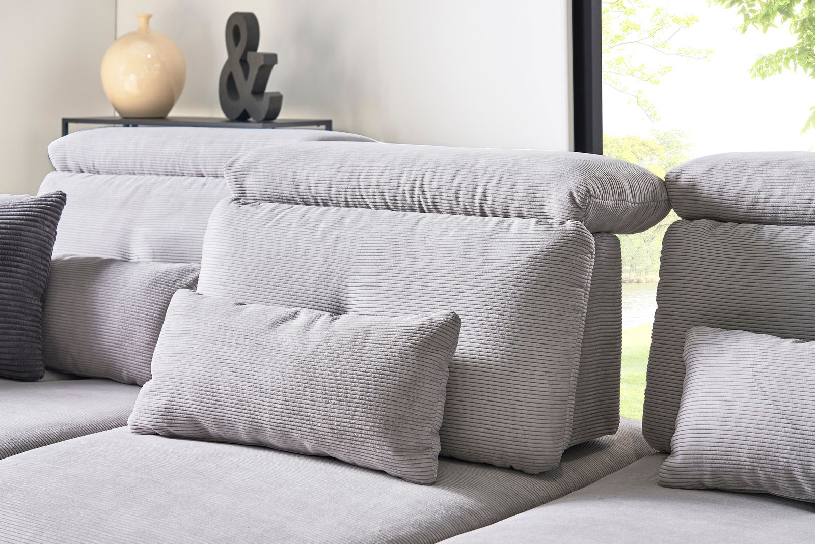 Graue Rundecke mit verstellbaren Kopfstützen und Kissen, seitliche Perspektive