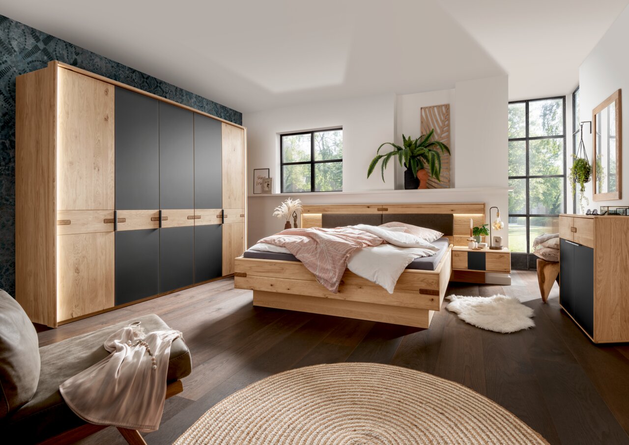 Modernes Schlafzimmer mit Holz-Kleiderschrank, Bett und Kommode in einer hellen, gemütlichen Atmosphäre. Perspektive von der linken Seite des Raumes.
