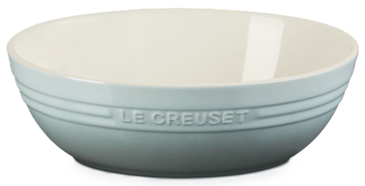 Hellblaue Le Creuset Keramikschüssel mit geprägtem Logo und weißer Innenfläche, seitliche Frontansicht vor weißem Hintergrund