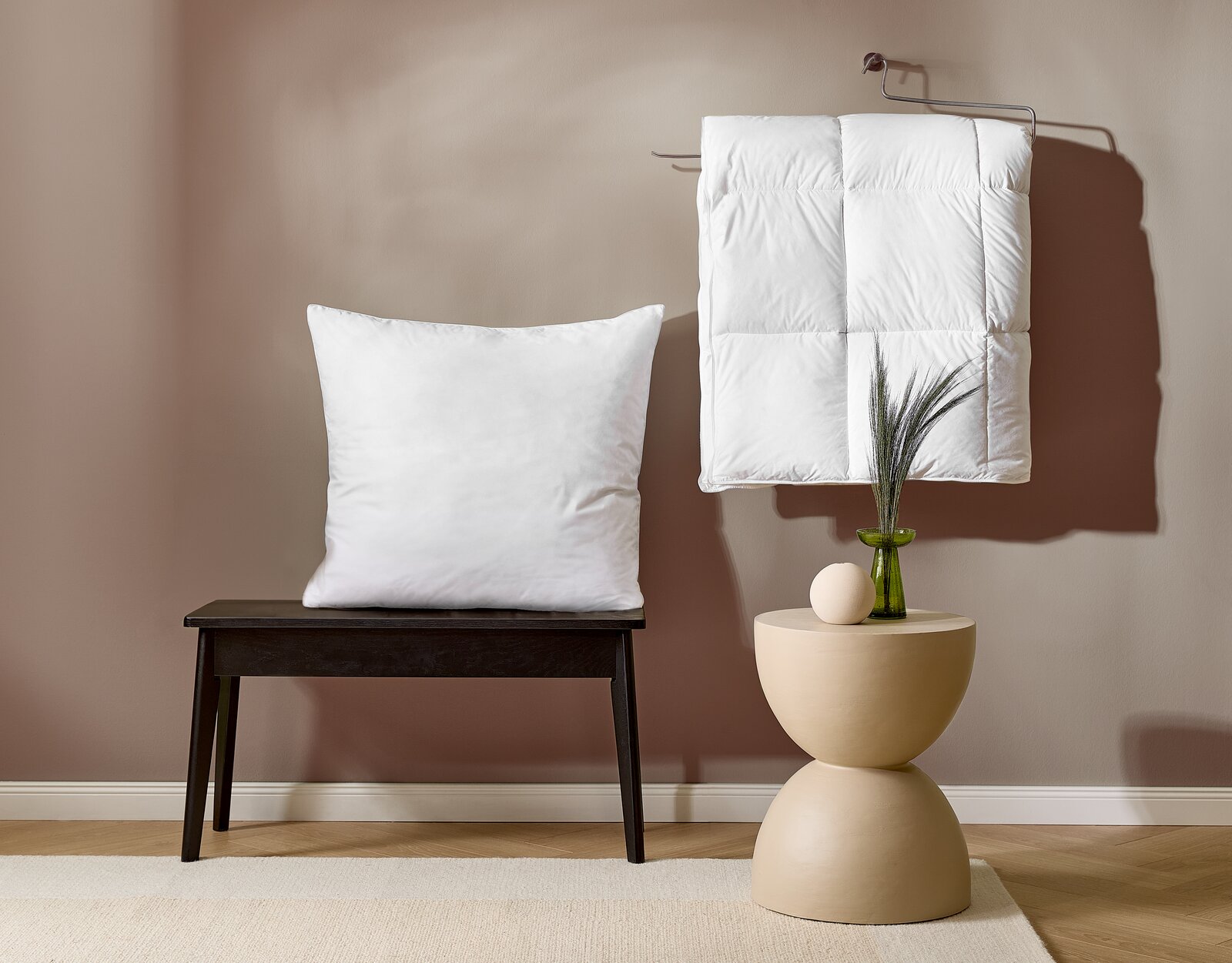 Ein weißes Kopfkissen auf einer schwarzen Bank und eine weiße Daunendecke, die an einem Haken hängt. Perspektive von vorne.