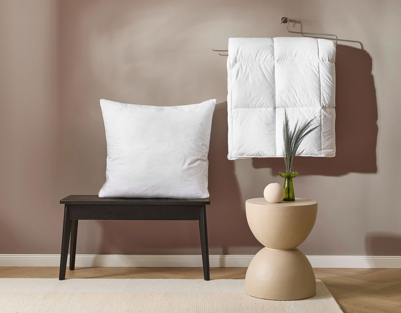 Ein weißes Kopfkissen auf einer schwarzen Bank und eine weiße Daunendecke, die an einem Haken hängt. Perspektive von vorne.