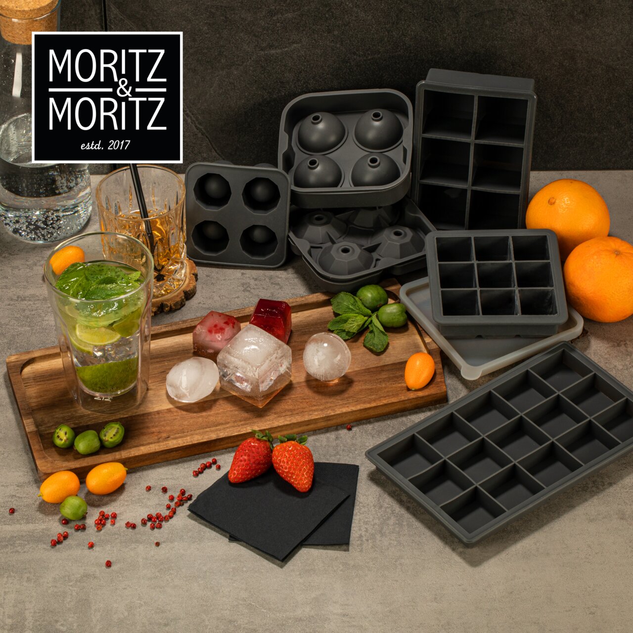 Verschillende ijsblokjesvormpjes in de vorm van diamanten en bolletjes op een tafel, omringd door drankjes, fruit en kruiden. Aanzicht van bovenaf.