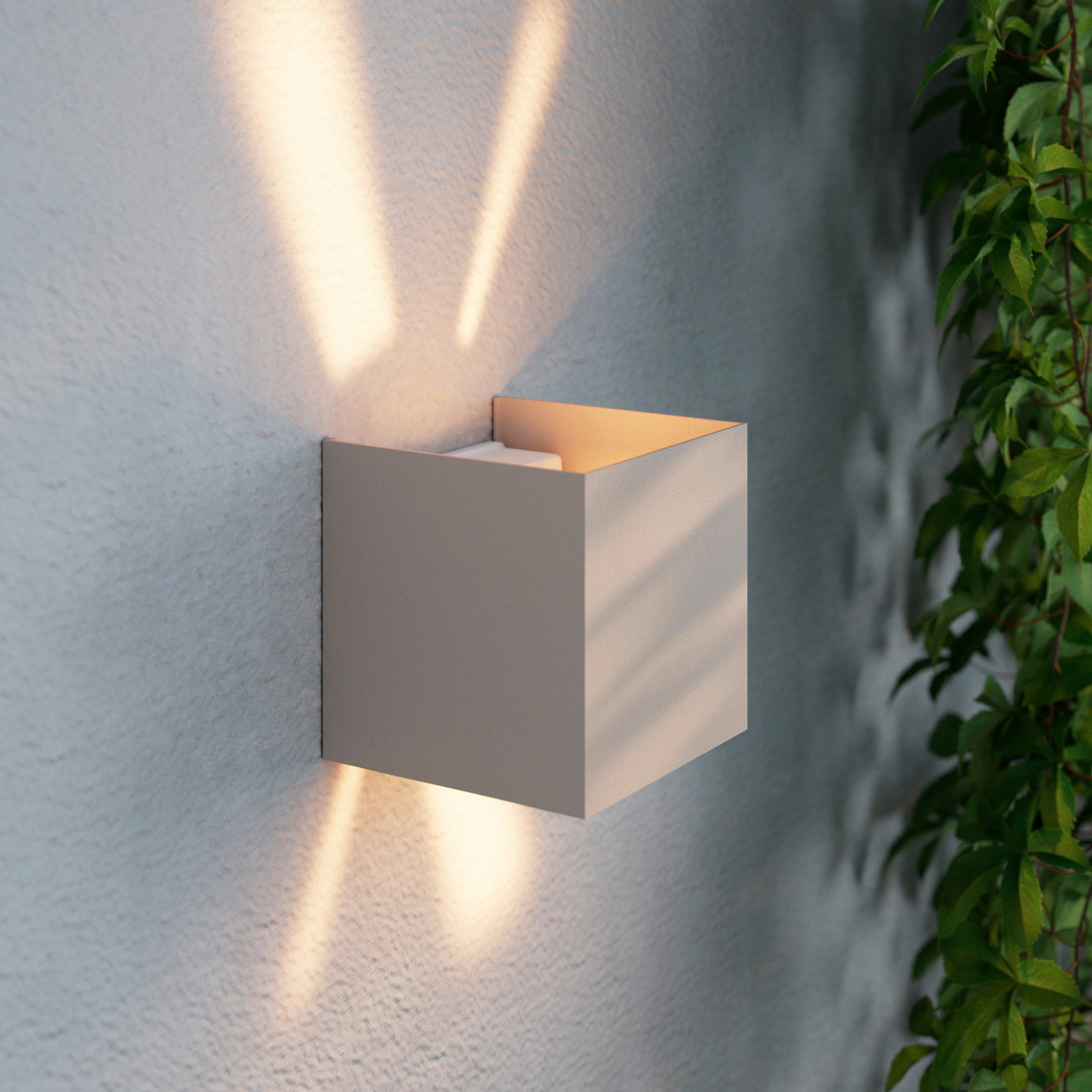 Moderne LED-Wandleuchte in kubischer Form, seitliche Perspektive, mit warmem Lichtstrahl nach oben und unten an einer strukturierten Wand.