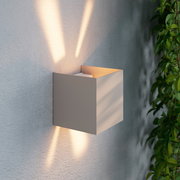 Moderne LED-Wandleuchte in kubischer Form, seitliche Perspektive, mit warmem Lichtstrahl nach oben und unten an einer strukturierten Wand.